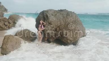 慢动作，漂亮的年轻女孩，穿着泳衣，站在大海和海浪<strong>背景</strong>下的大石头附近，<strong>稳重</strong>的。